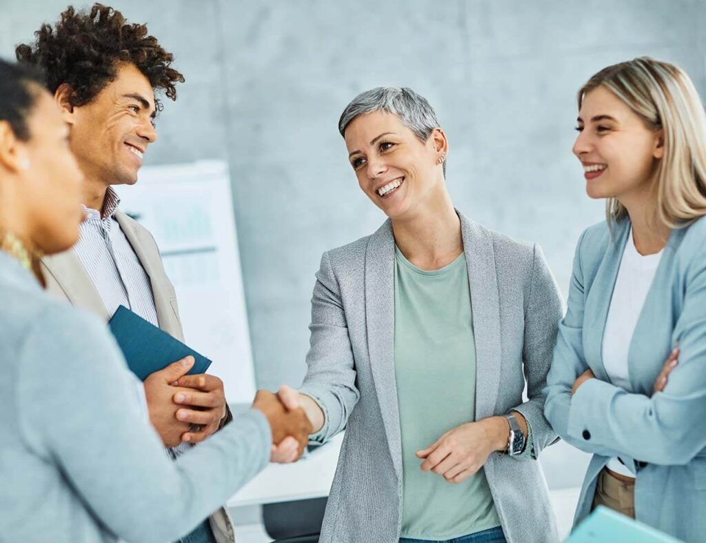 Group of diverse business professionals, including employment lawyers, smiling and shaking hands during a meeting in an office setting.