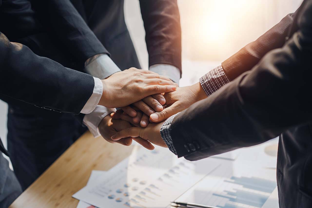 Commercial Lawyers Melbourne 2 Team Of Business Professionals In Formal Attire Placing Their Hands Together In A Show Of Unity And Collaboration Over A Table With Business Documents.