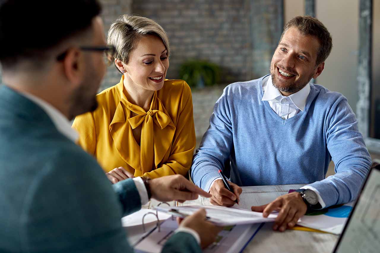 Binding Financial Agreements 11 A Smiling Couple Signing Documents With A Professional, Symbolising Clarity And Agreement In Legal Matters.